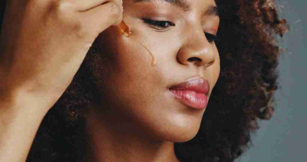 african american woman using a dropper of skincare serum
